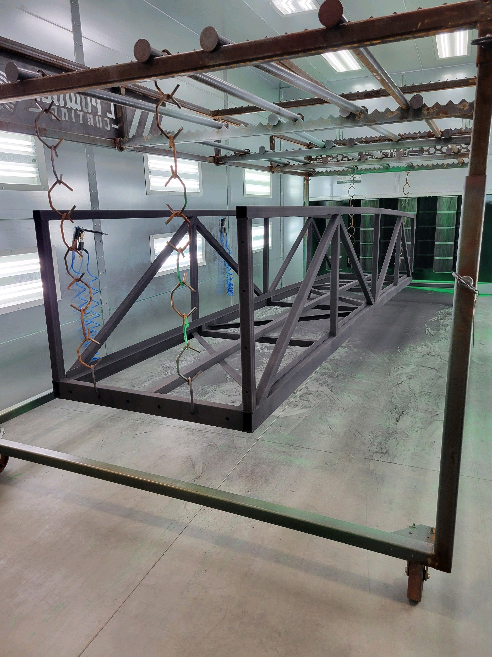 A large metal structure is being painted in a paint booth.