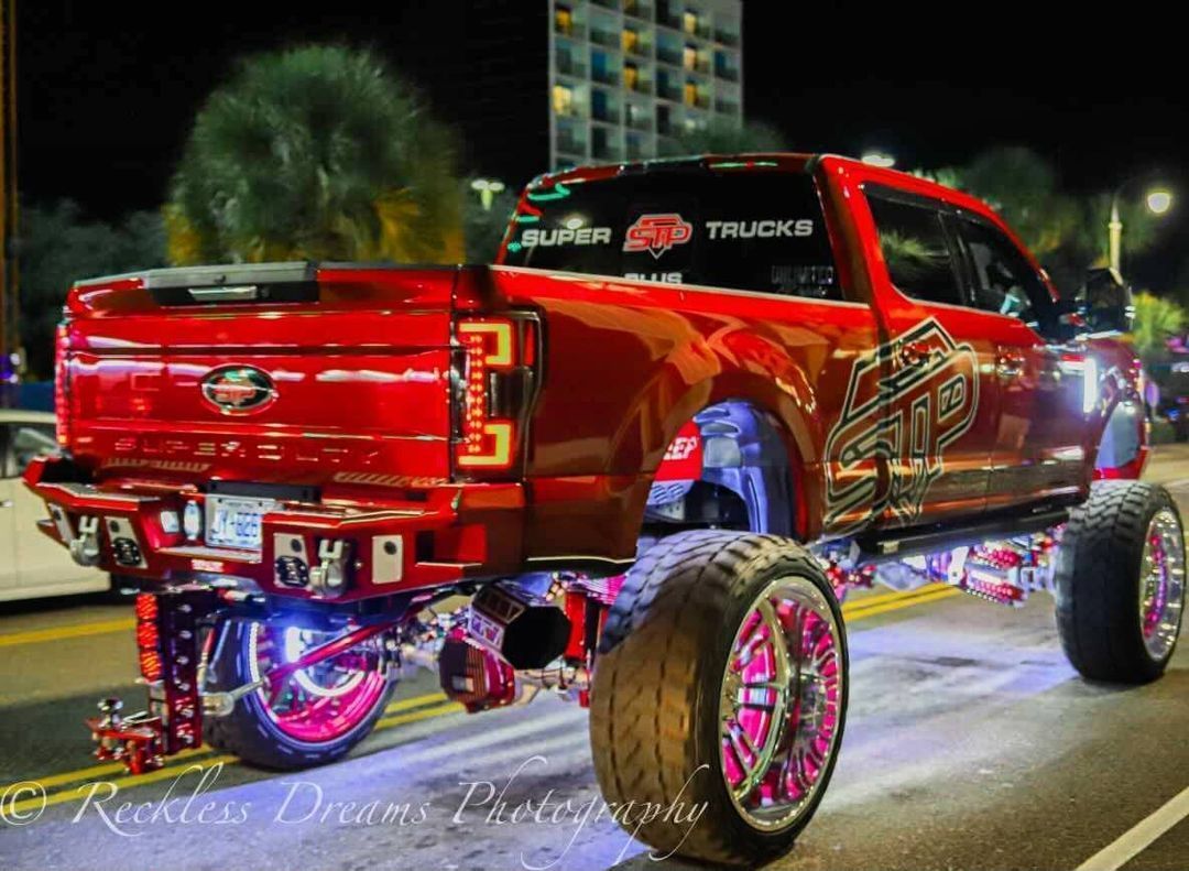 A red truck with pink wheels is parked on the side of the road at night.