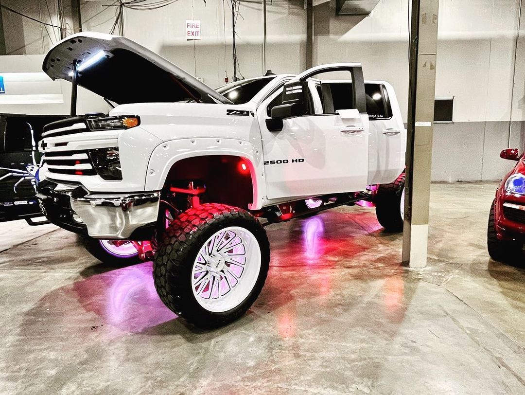 A white truck with the hood up is parked in a garage.
