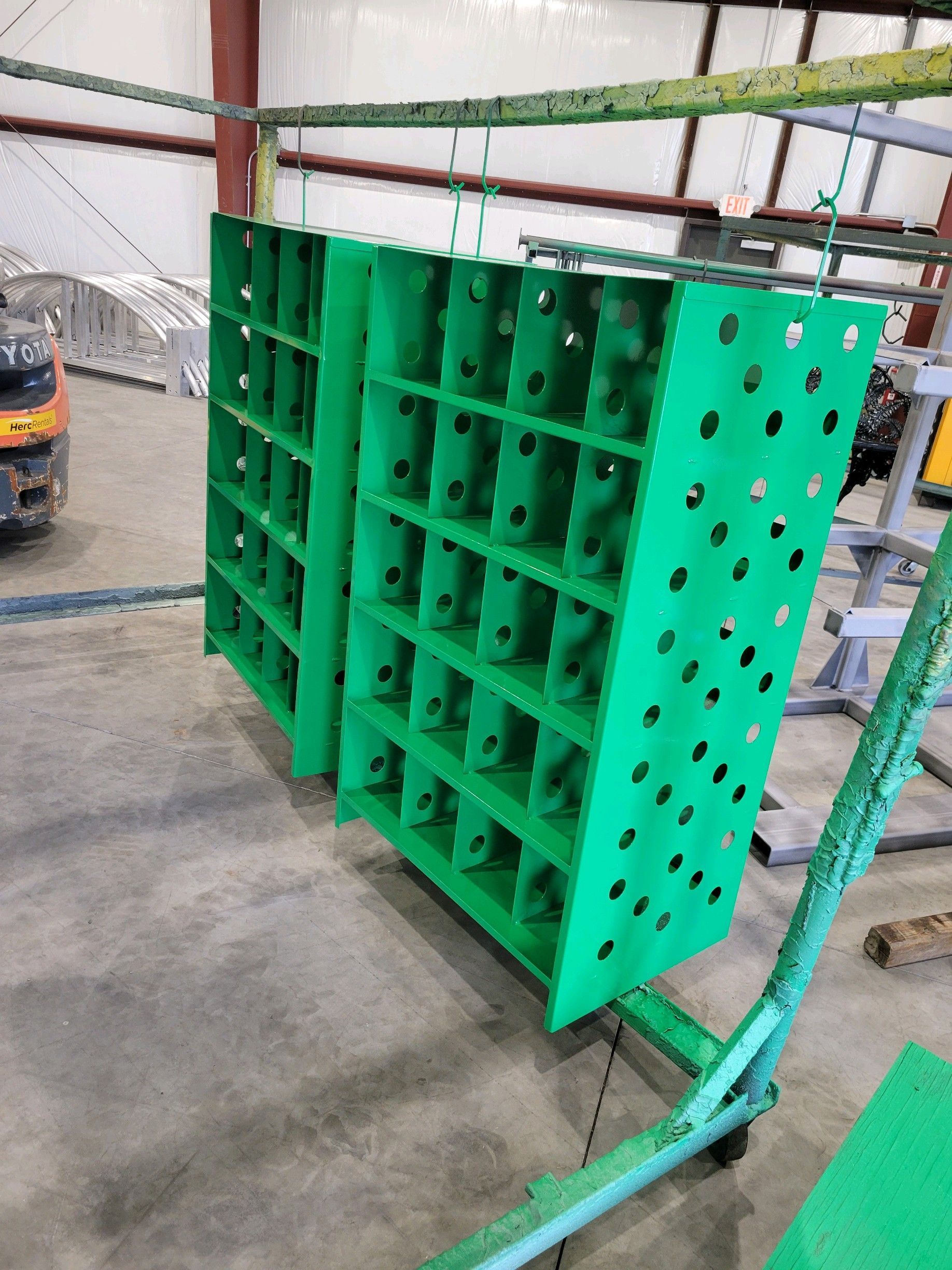 A green shelf with holes in it is sitting in a warehouse.