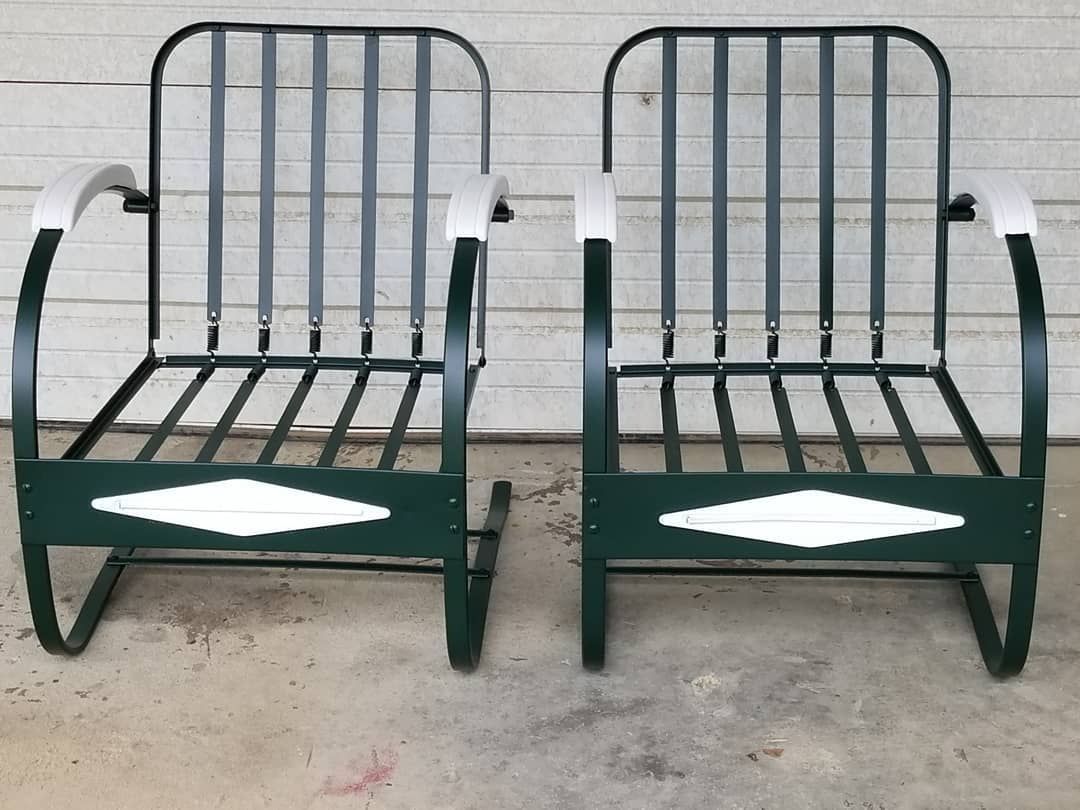 A pair of green metal rocking chairs with white arm rests