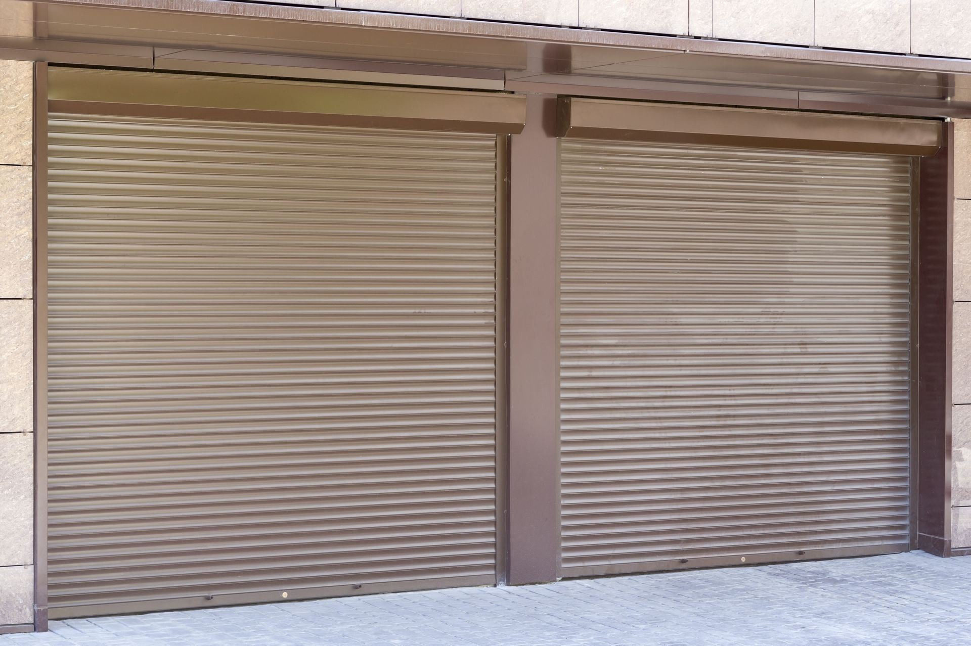 Two closed, brown, horizontal-slat rolling shutters on a building.