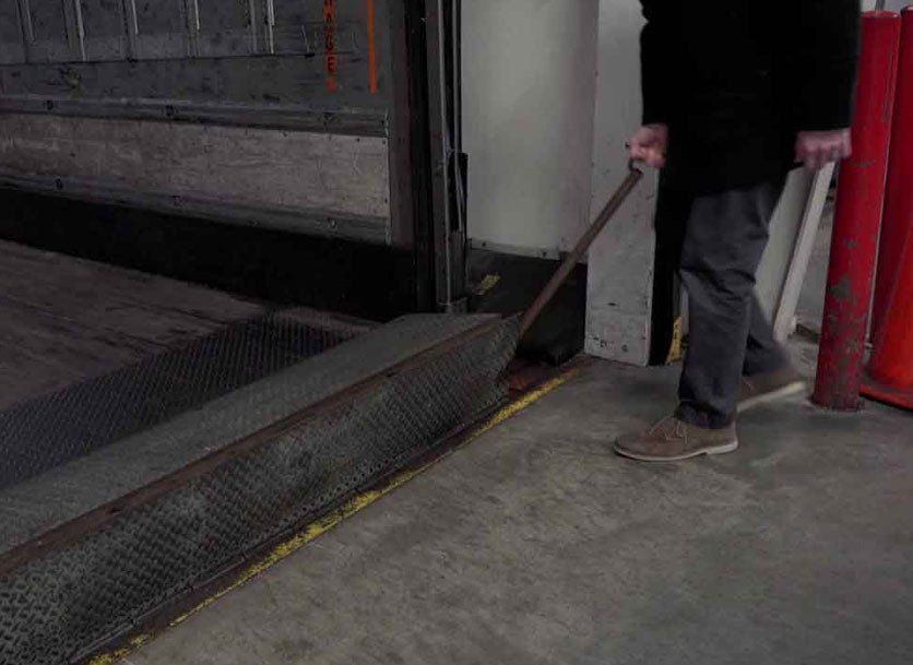 Person uses a rod to move a metal ramp at a loading dock.