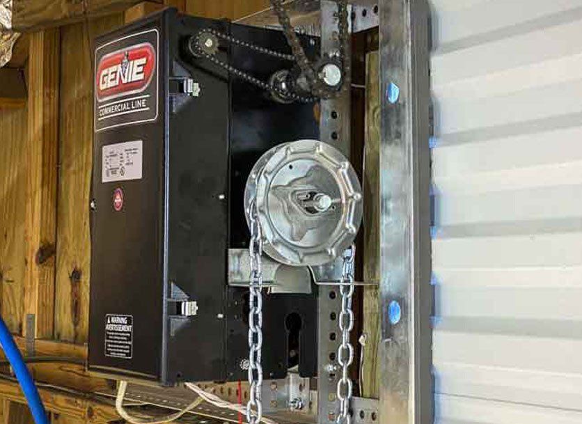 Black Genie garage door opener mounted on a metal frame. Chain and sprocket visible.