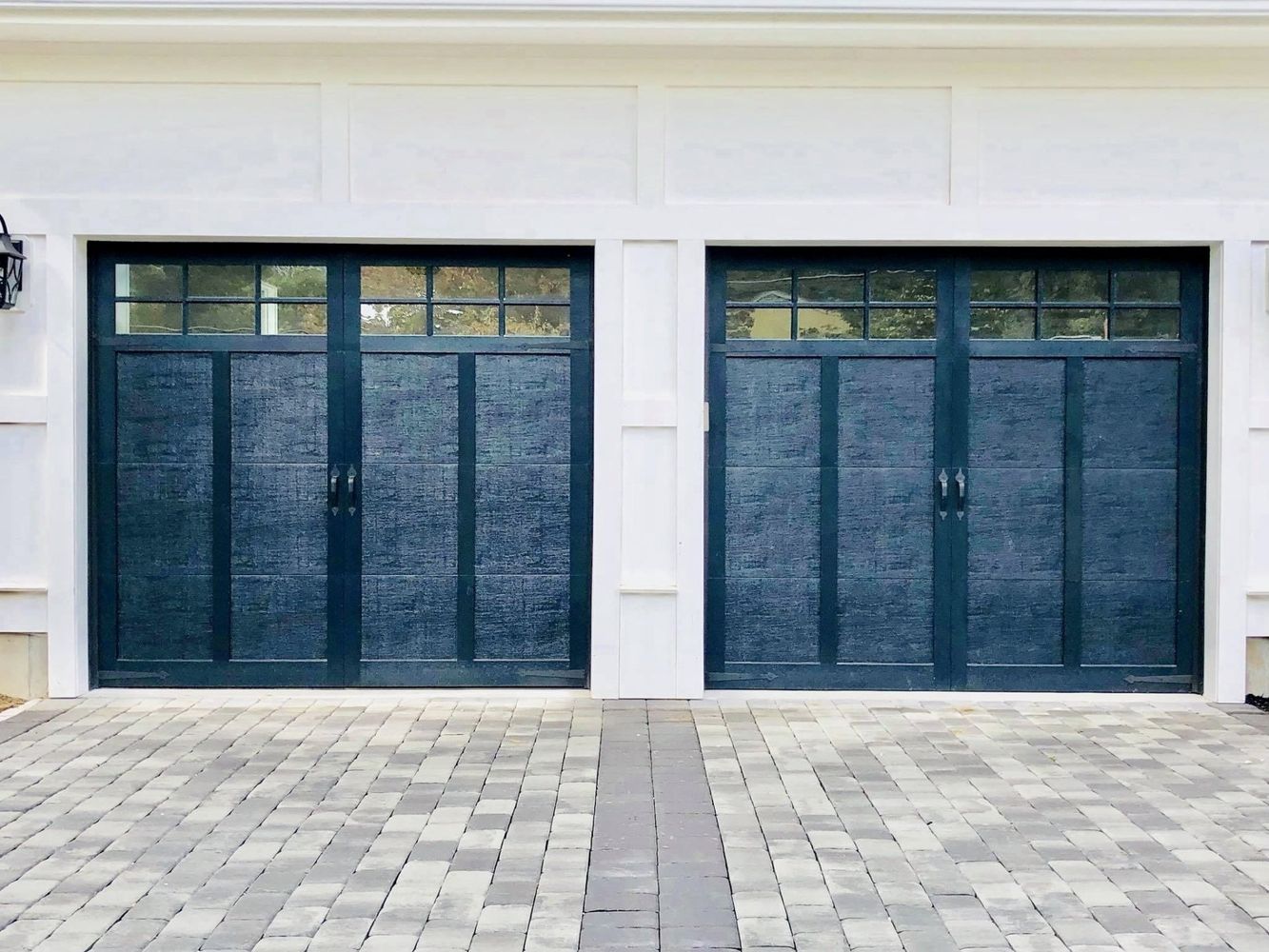 Two dark blue garage doors with glass panel tops, facing brick paved driveway.