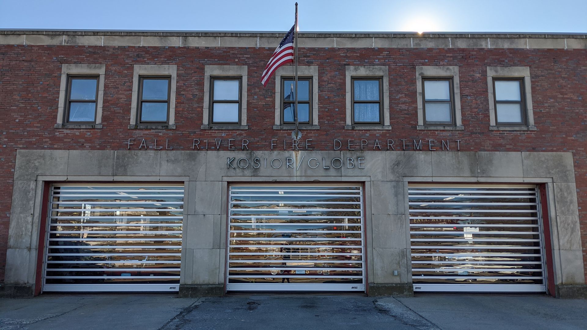 Fire station with three garage doors, brick exterior, American flag.