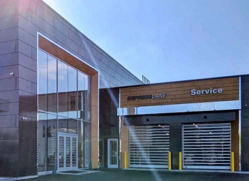 Modern auto service center with glass entrance, service bay doors, and signage.
