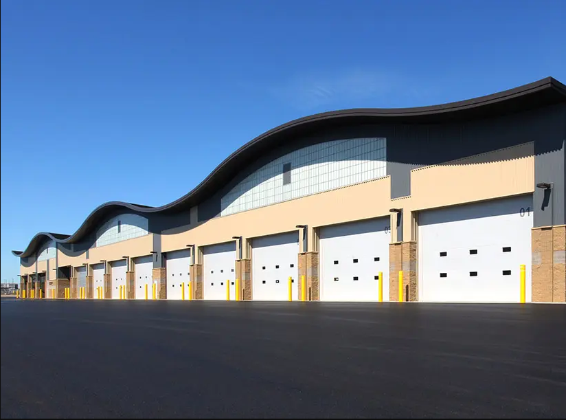 Large warehouse with multiple white garage doors, curved roof, and blue sky.
