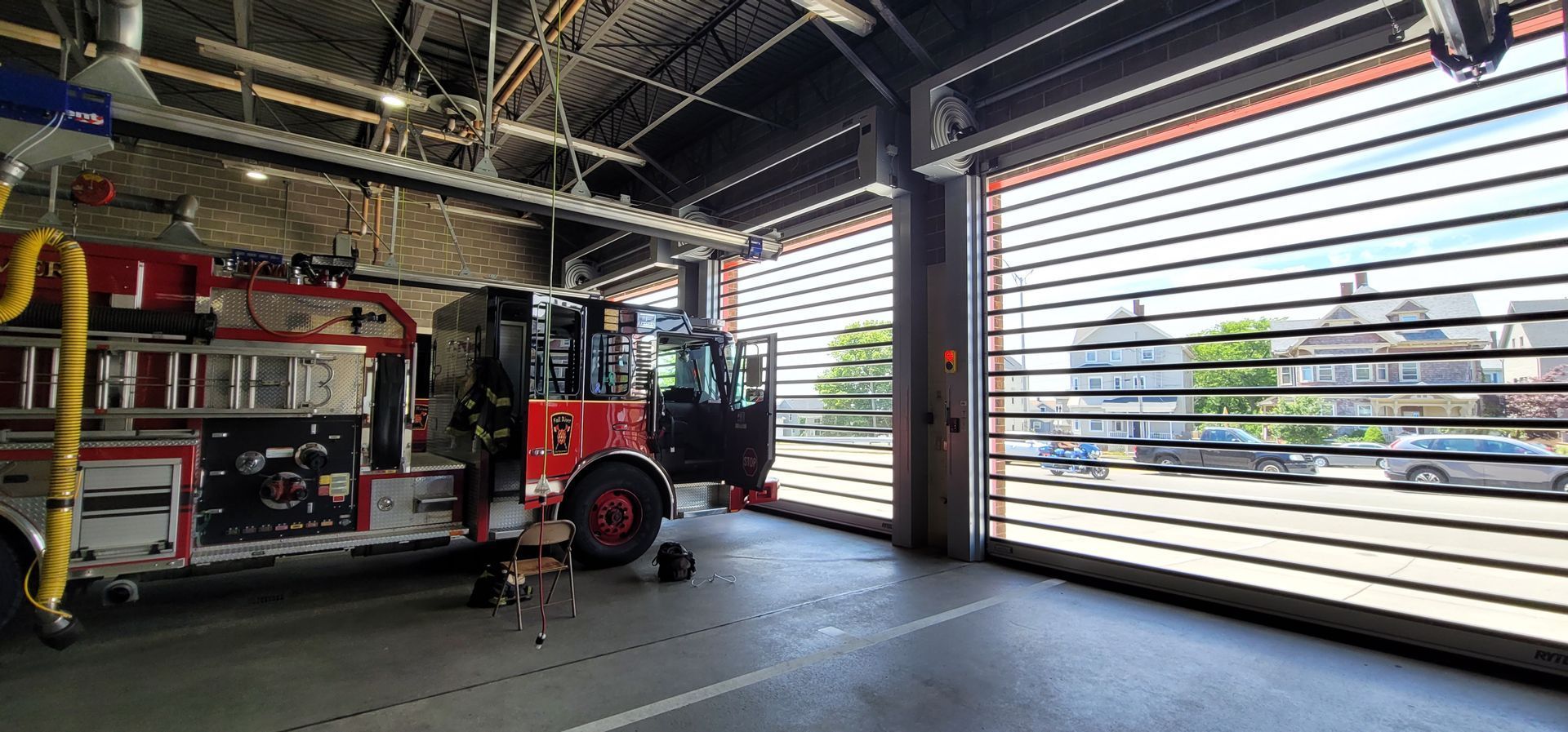 Fire engine inside a fire station, with the open door revealing street view.