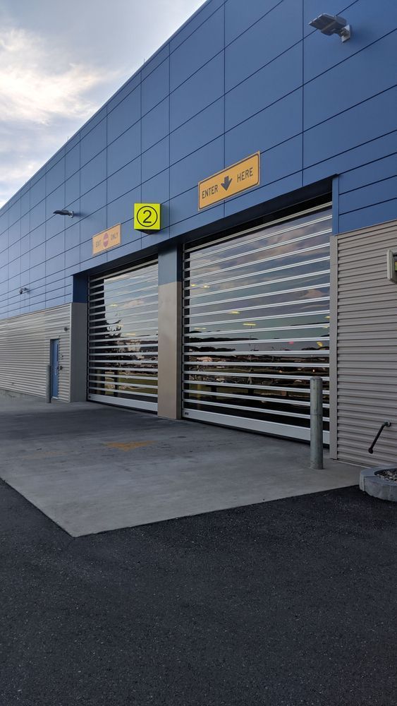 Blue building with two garage doors partially open. Metal grates and reflective glass panes.