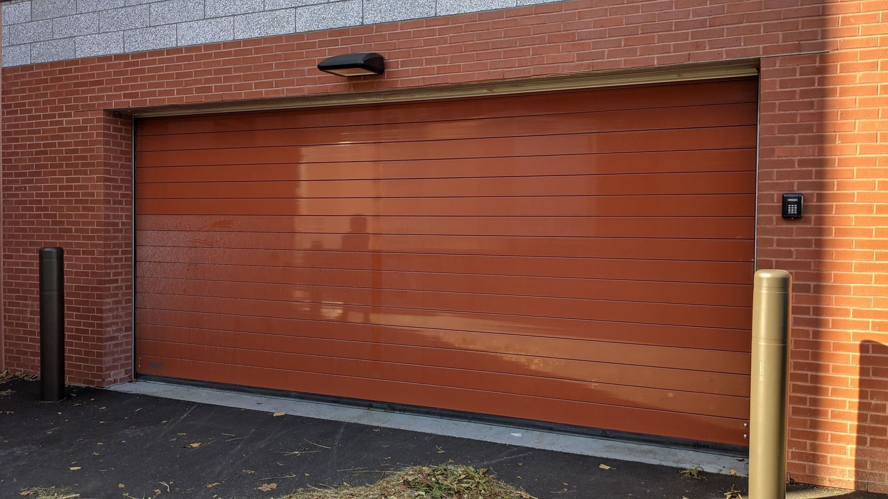 Brown garage door, brick building exterior, bollards, security keypad.