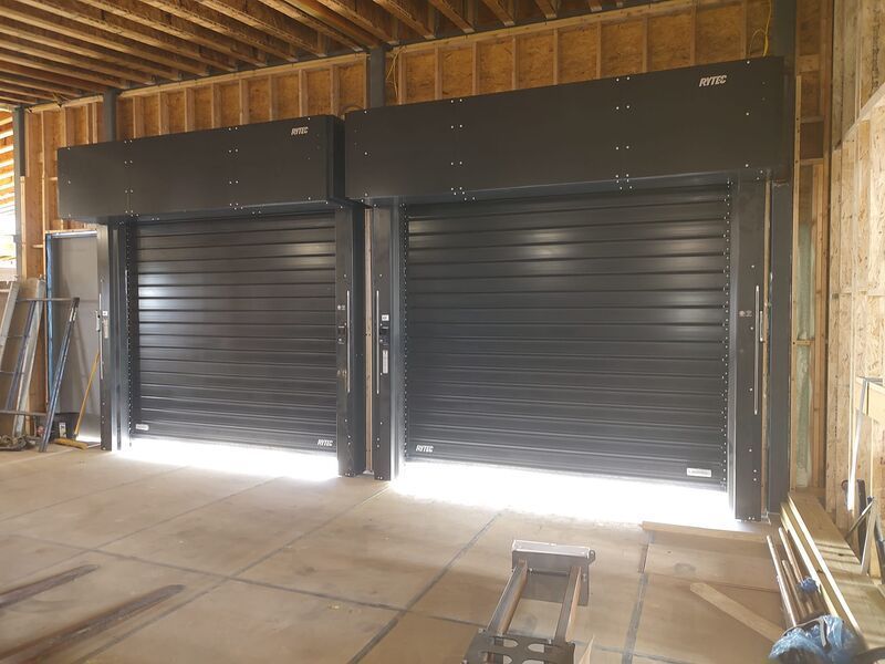 Two black garage doors with dark overhead boxes in a building under construction.