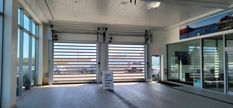 Interior of a building with two large garage doors open. A sign in front says “Please wait to be seated.”