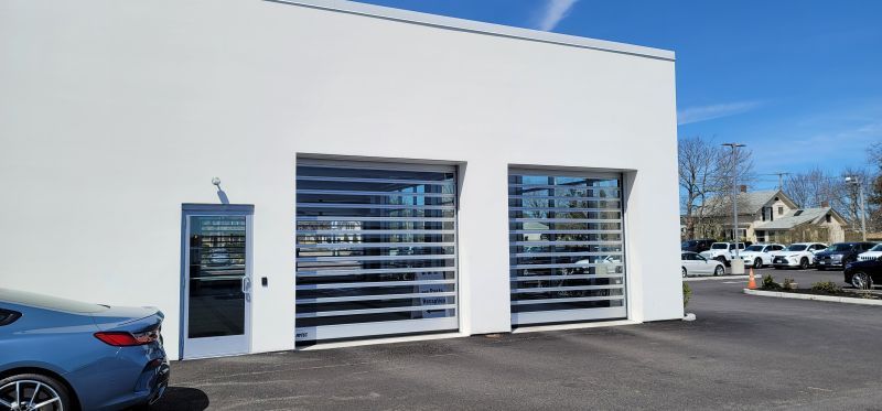 White building with glass garage doors and a blue car parked in front.