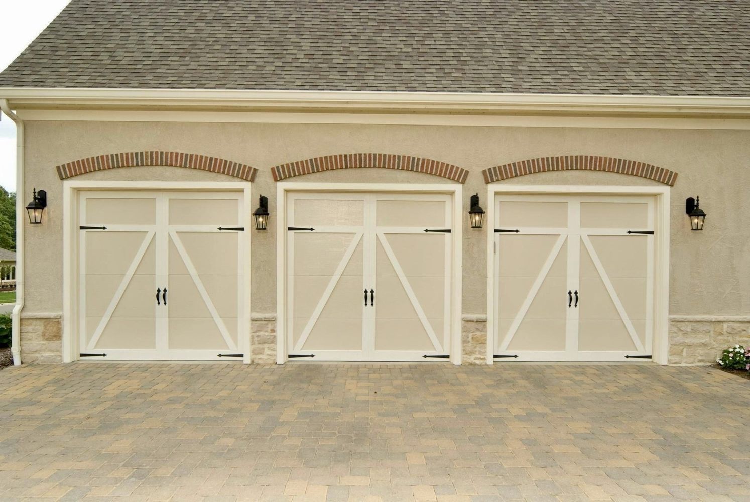 Three white garage doors with arched brick detail, black hardware, set in a tan stucco facade.