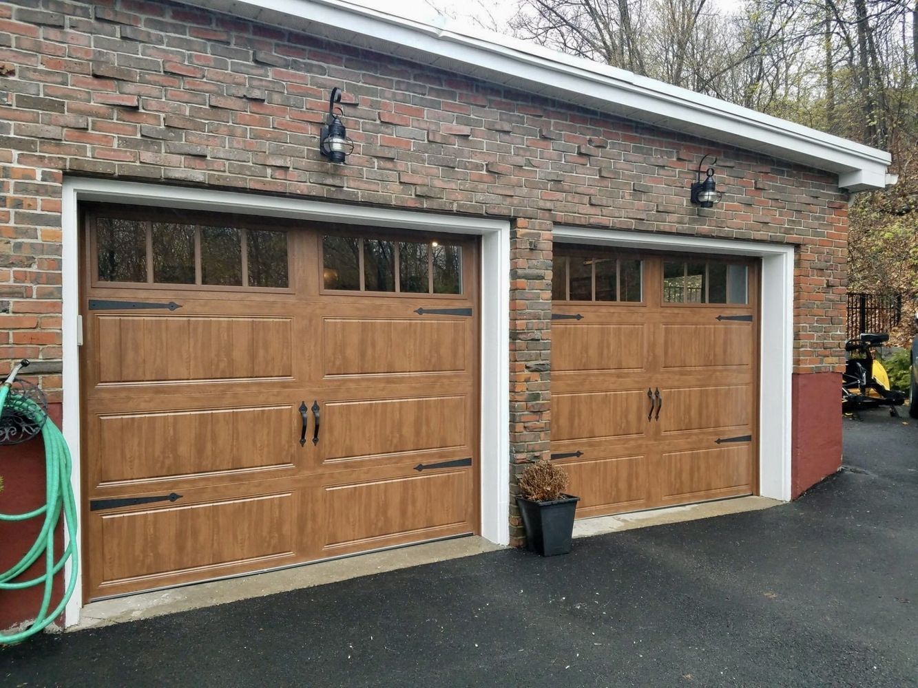 Two brown garage doors on a brick building with black hardware, with overhead lighting.