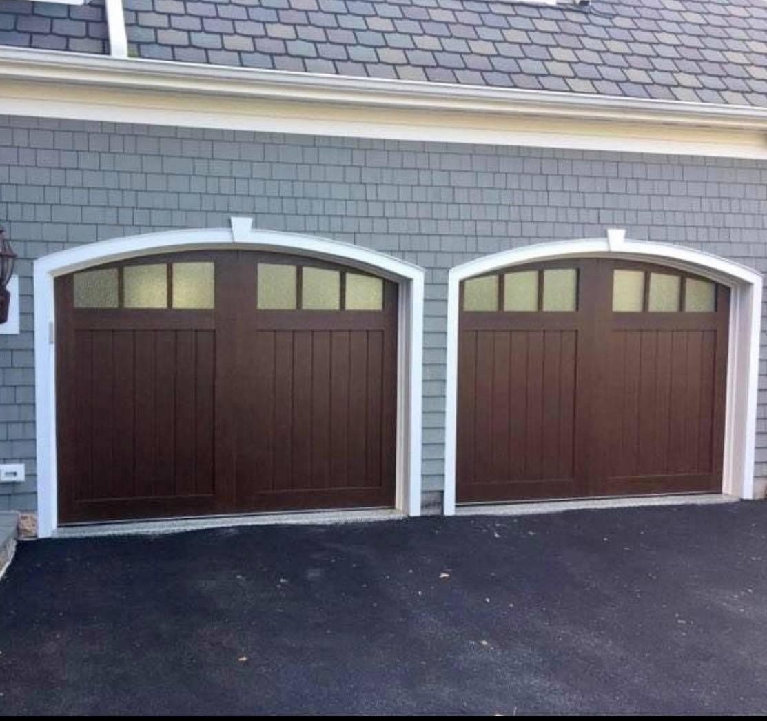 Brown garage doors with arched windows in white trim, set against gray siding.