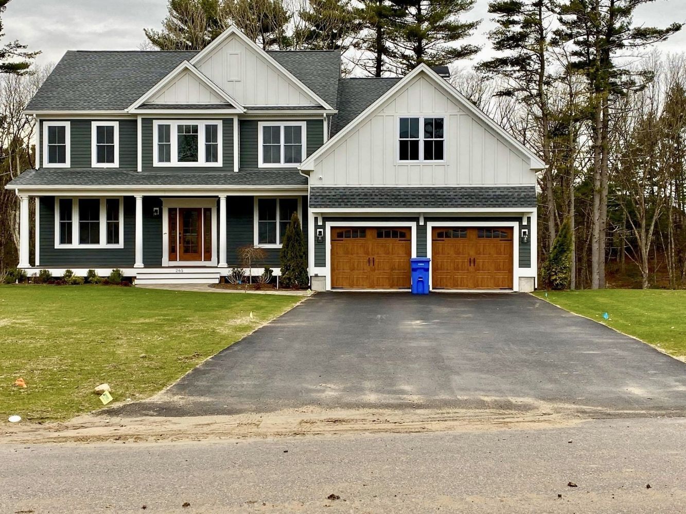 Two-story house with green siding, white trim, and a two-car garage with brown doors. Asphalt driveway, green lawn.