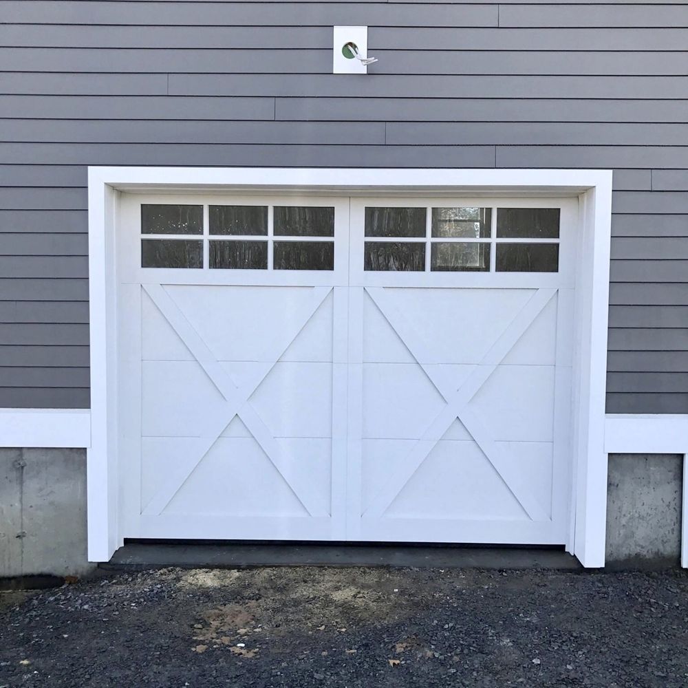 White garage door with glass paneling, set against gray siding.