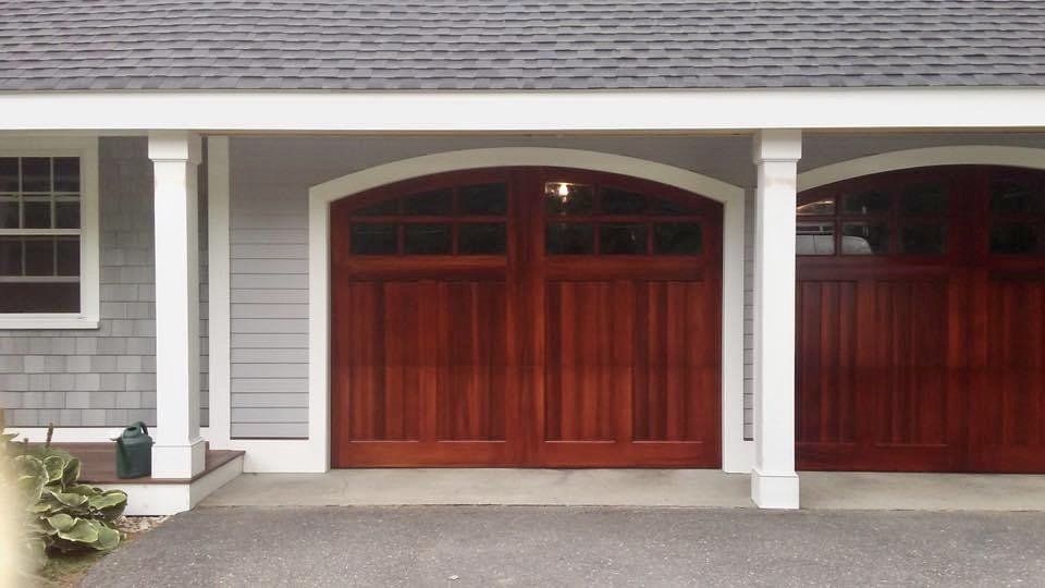 Wooden garage doors under a white covered porch with columns. Gray siding and a window on the left.
