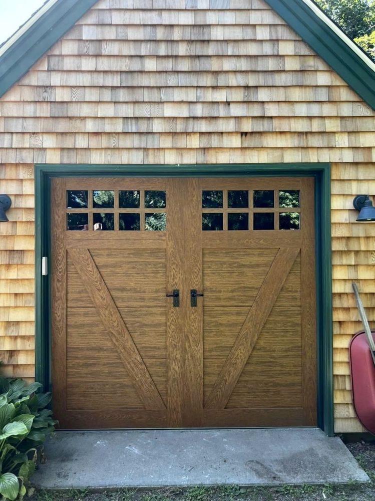 Brown garage doors with windows, green trim, and wooden siding.