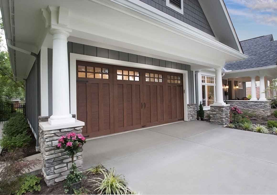 Garage with brown door, columns, and concrete driveway. Exterior of a house with grey siding.