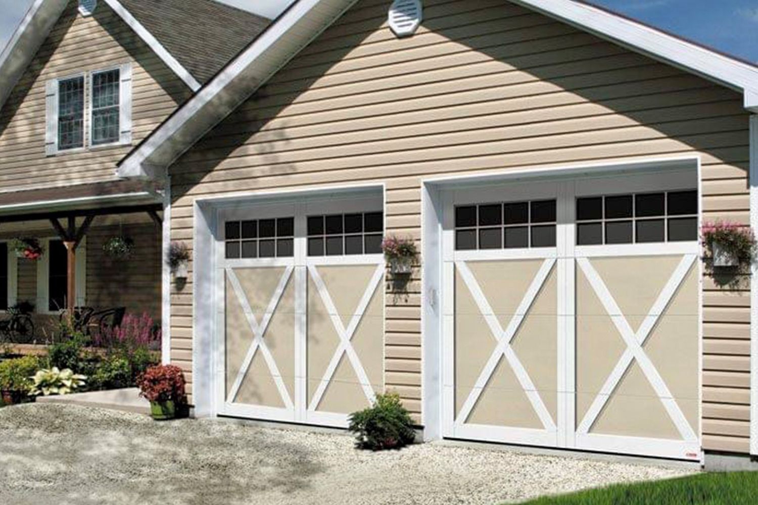 Two-car garage with tan siding and white trim. Garage doors are beige with white cross design and windows.