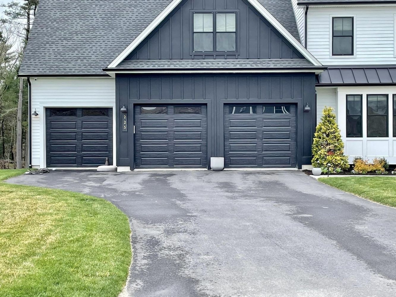 Black and white house with three dark gray garage doors and a paved driveway.