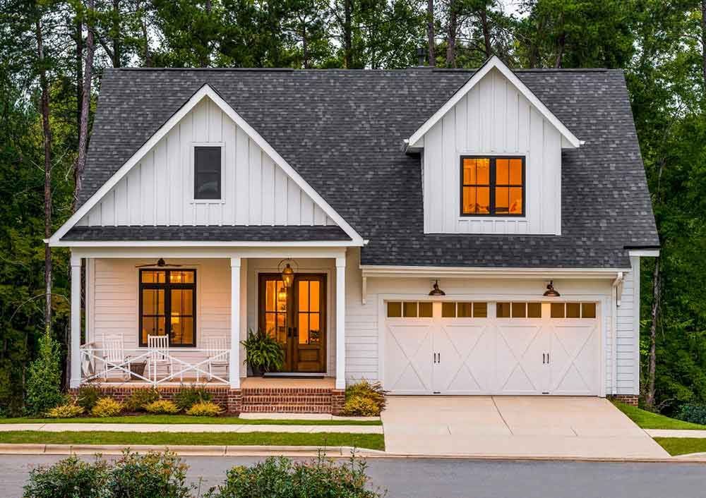White farmhouse with black roof, garage, porch, and windows.