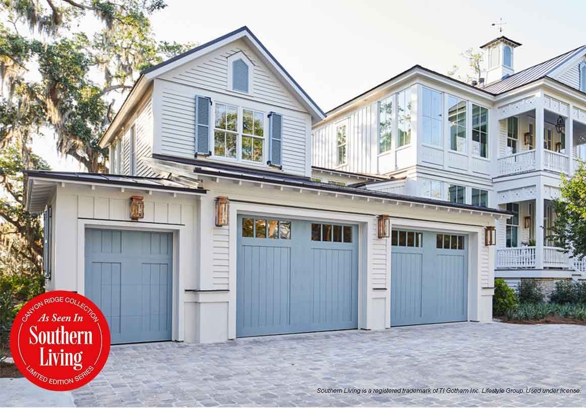 Three-car garage with light blue doors and white trim, next to a multi-story home with a porch.