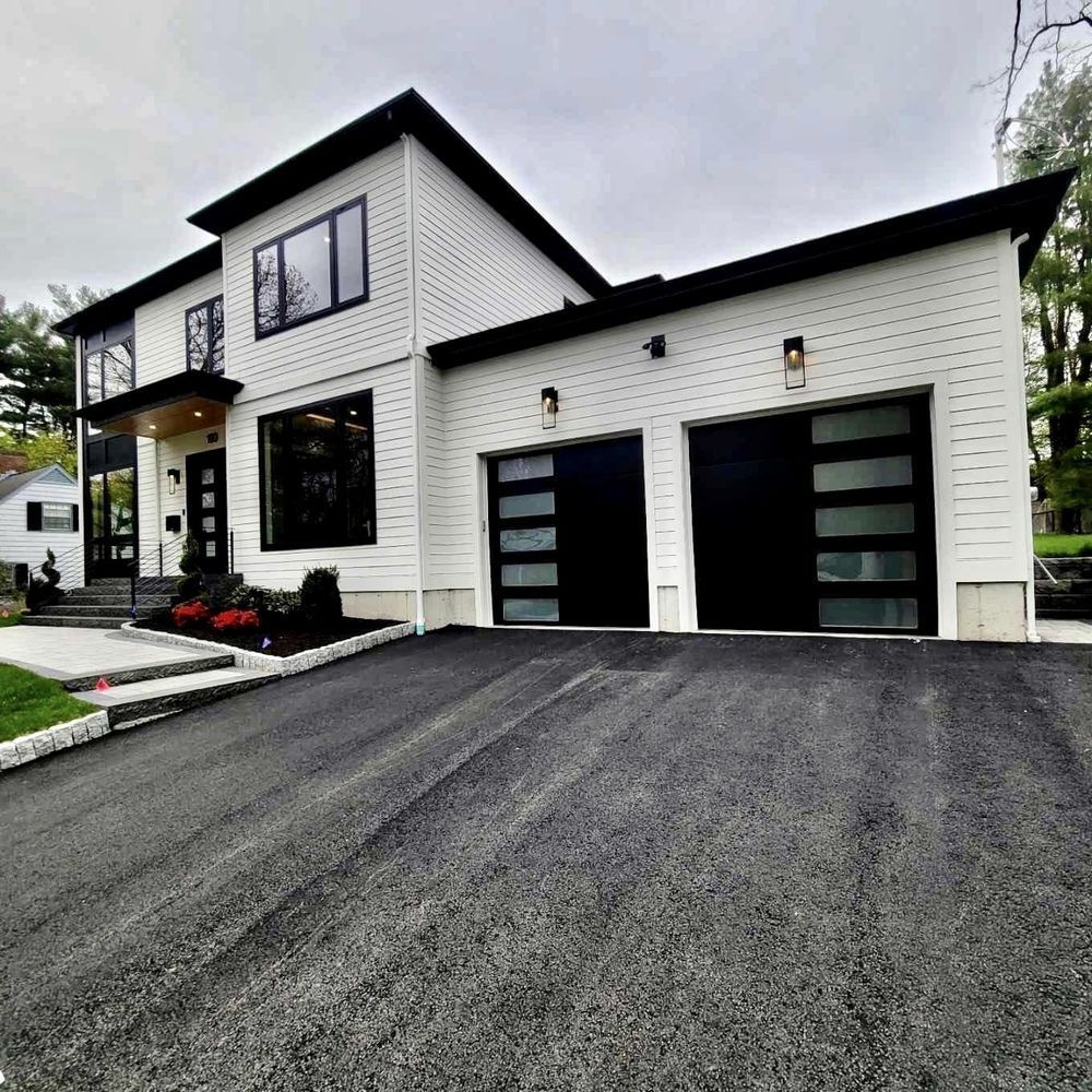 Modern white house with black garage doors, large windows, and an asphalt driveway.