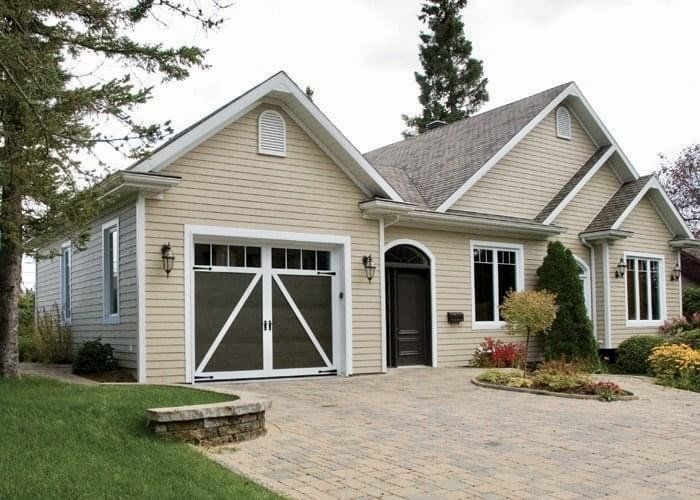 Beige house with a brown garage door, arched front door, and cobblestone driveway.
