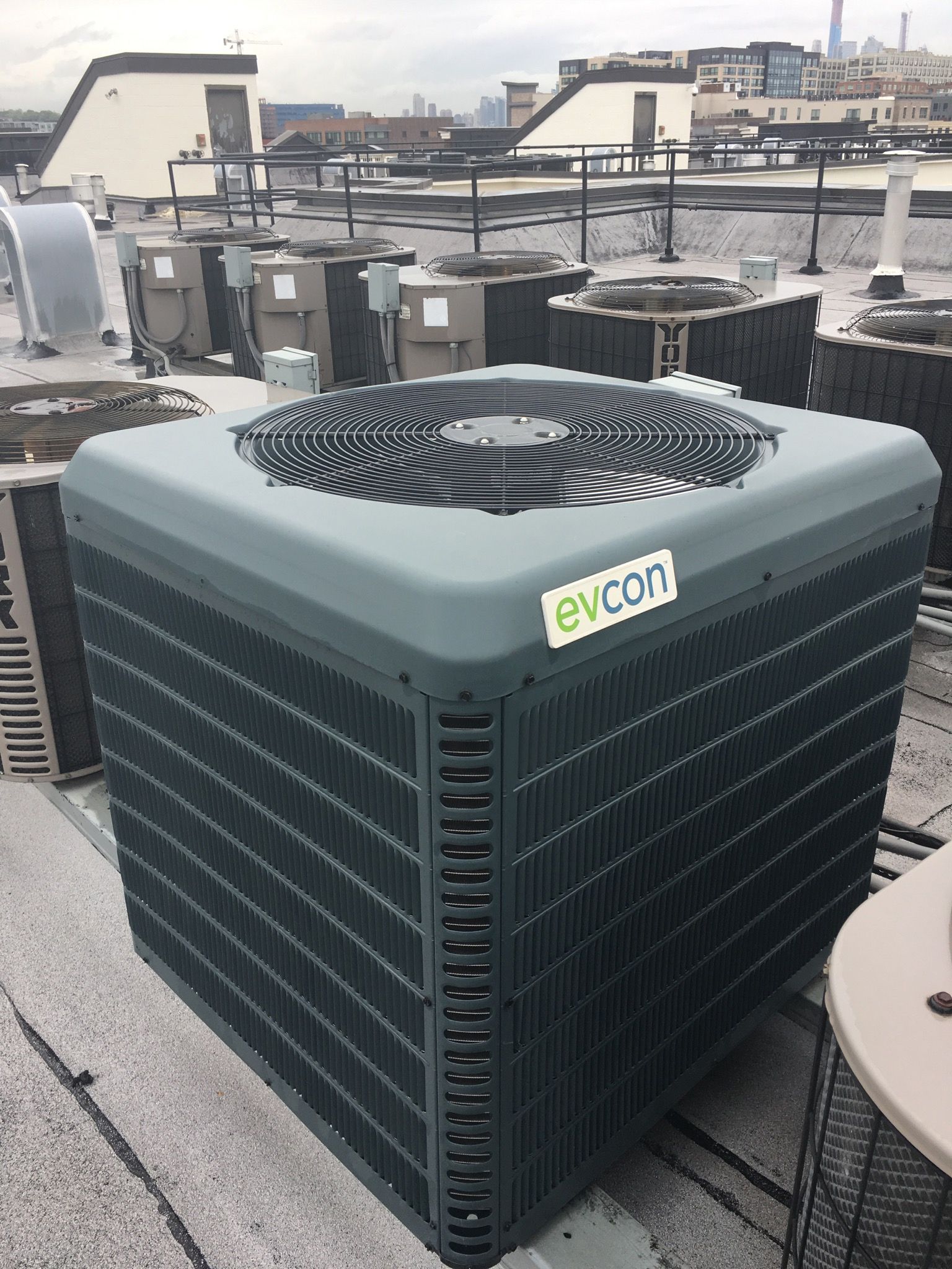Large green HVAC unit on a rooftop with city buildings and water in the background