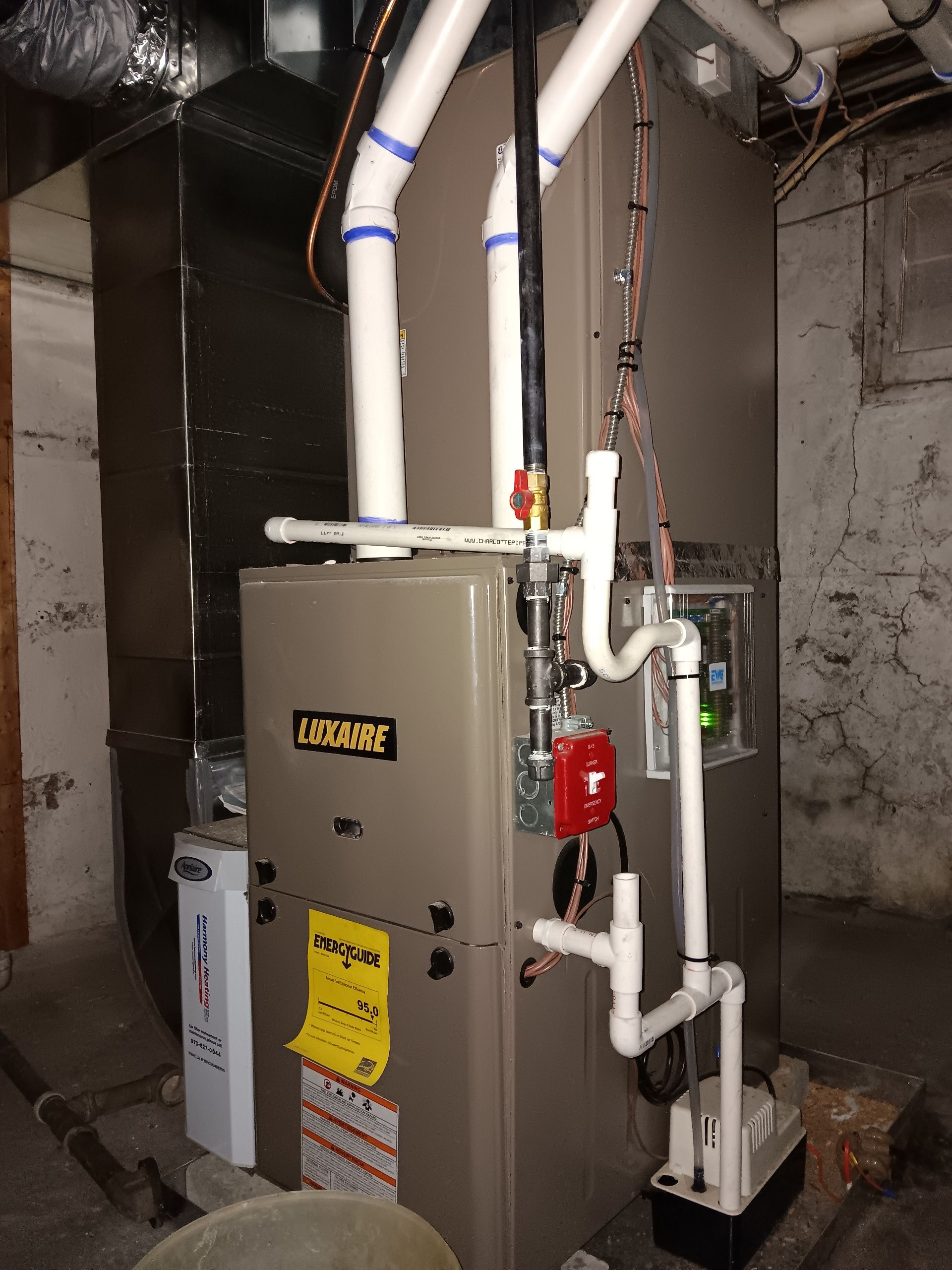 Gas furnace and ductwork in a basement utility room, with white pipes and a red pump attached.