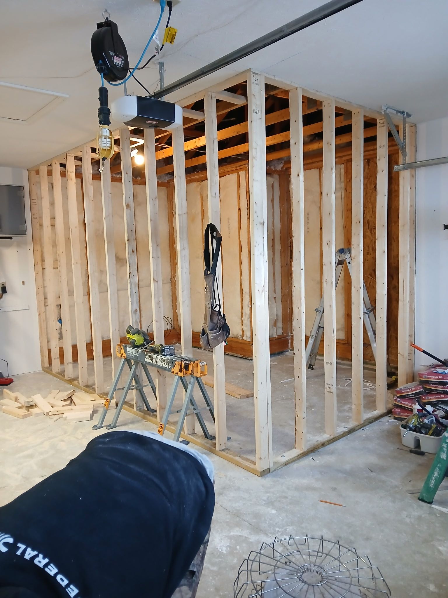 Framed wall under construction in a garage, with exposed studs, tools, and ladder.