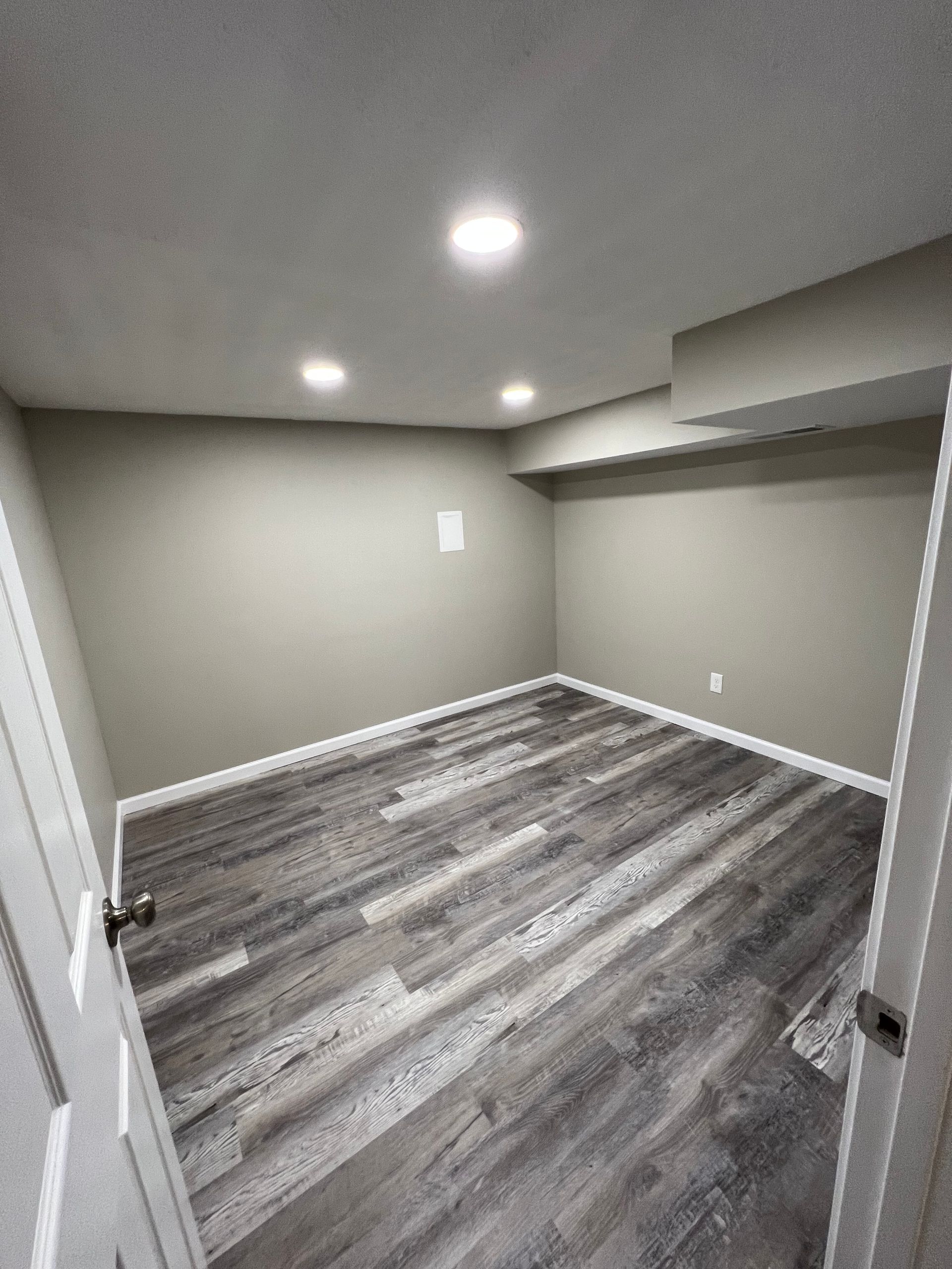 Empty gray room with wood-look flooring, recessed lights, and a built-in closet alcove.