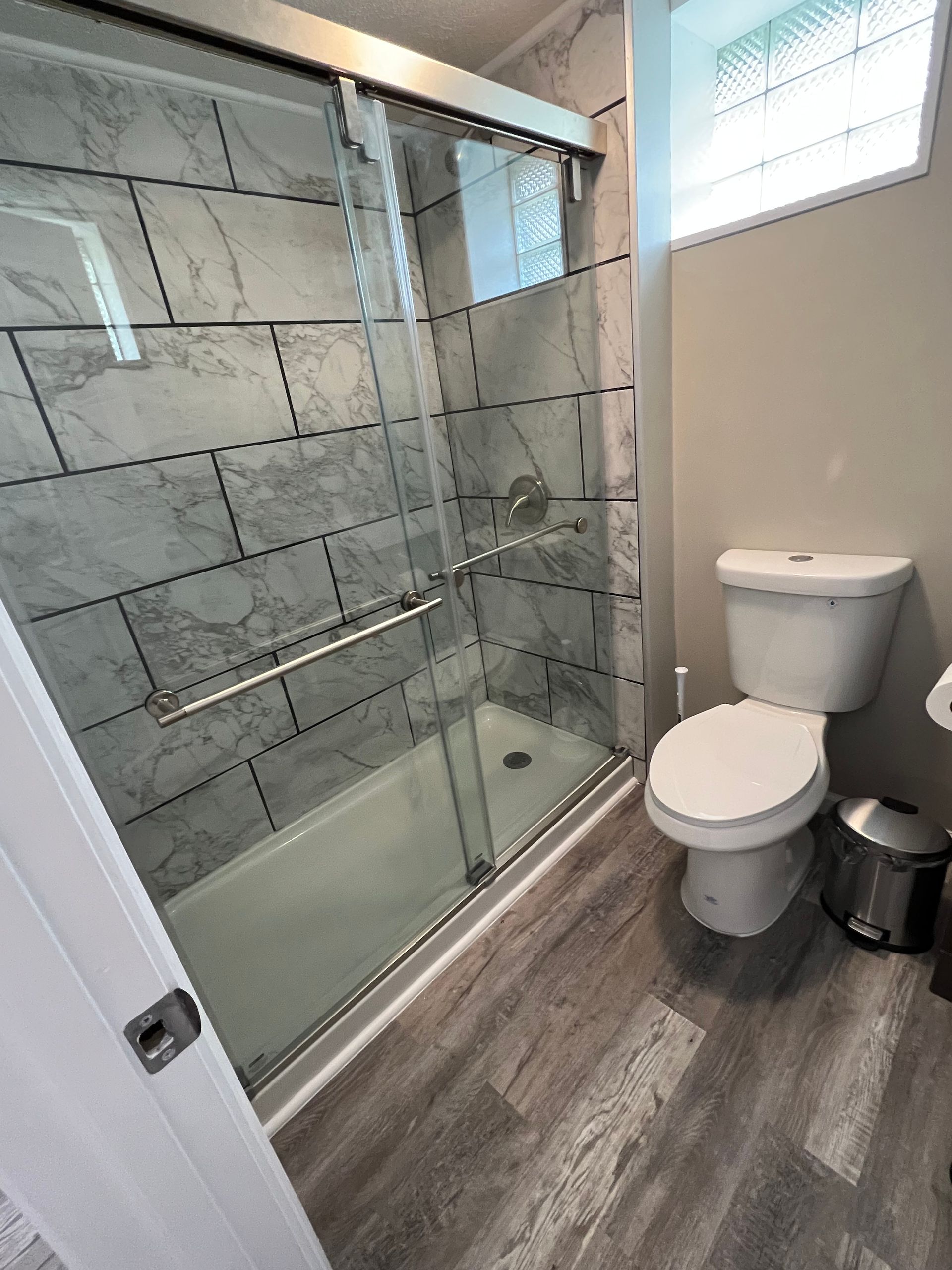 Modern bathroom with glass walk-in shower, toilet, and gray wood-look floor tiles.