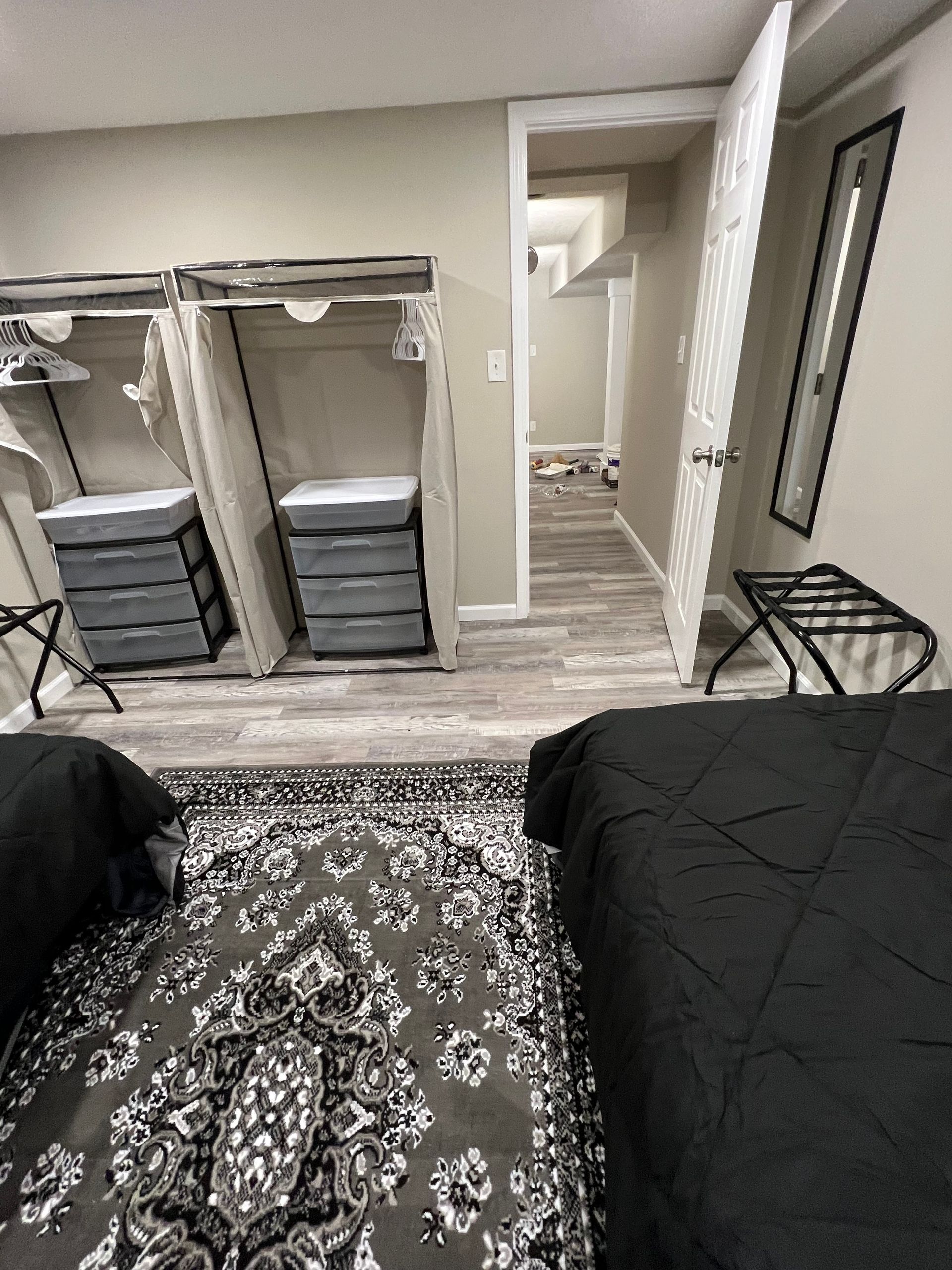 Modern bedroom with two beds, mirrored closet, dresser drawers, and a patterned rug, viewed from between the beds