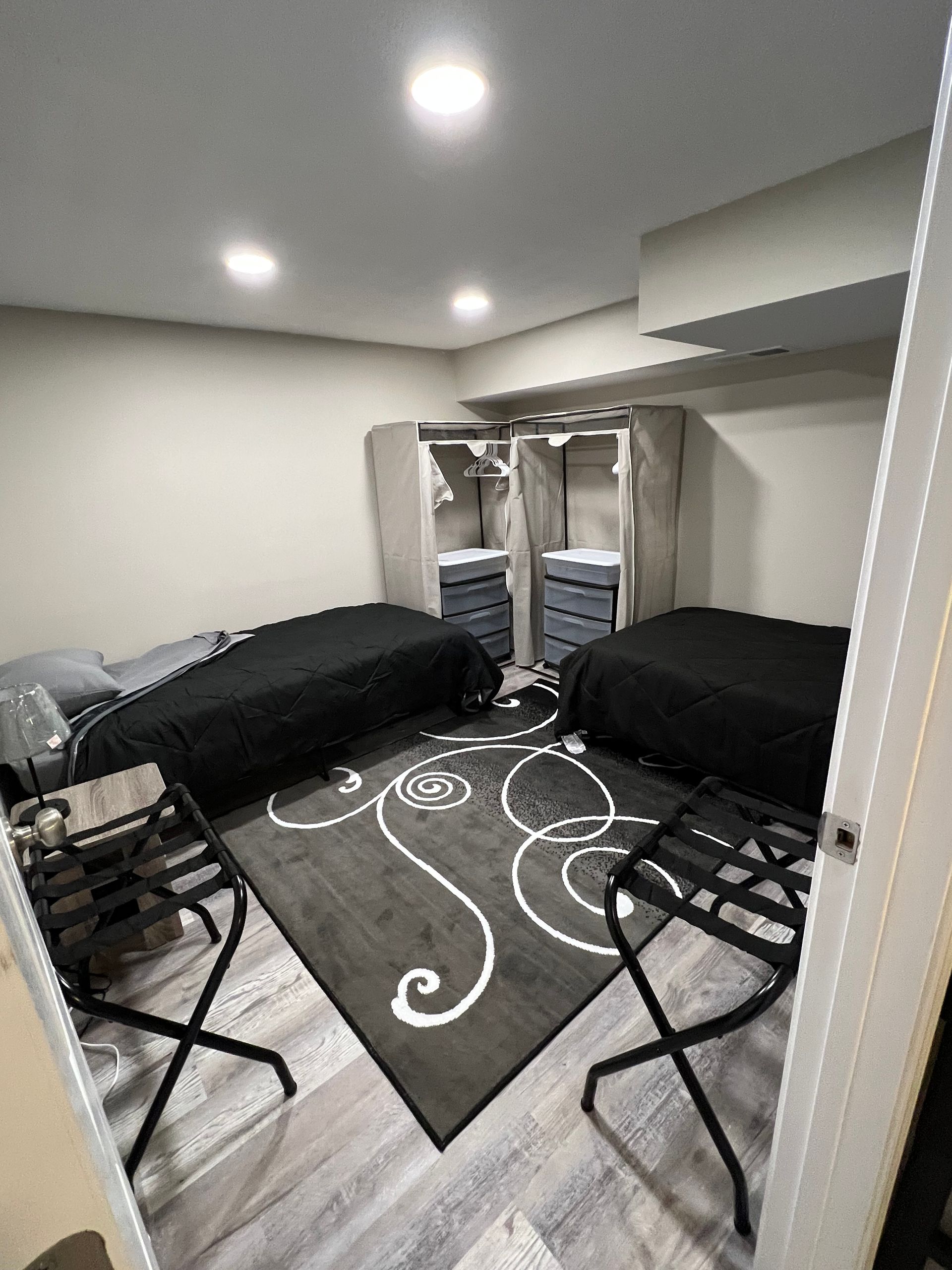 Small bedroom with two black futons, patterned gray rug, and an open closet with drawers.