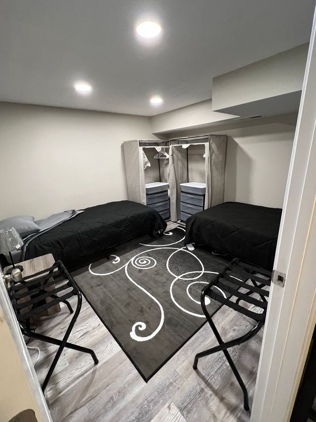 Small bedroom with two black futons, patterned gray rug, and an open closet with drawers.