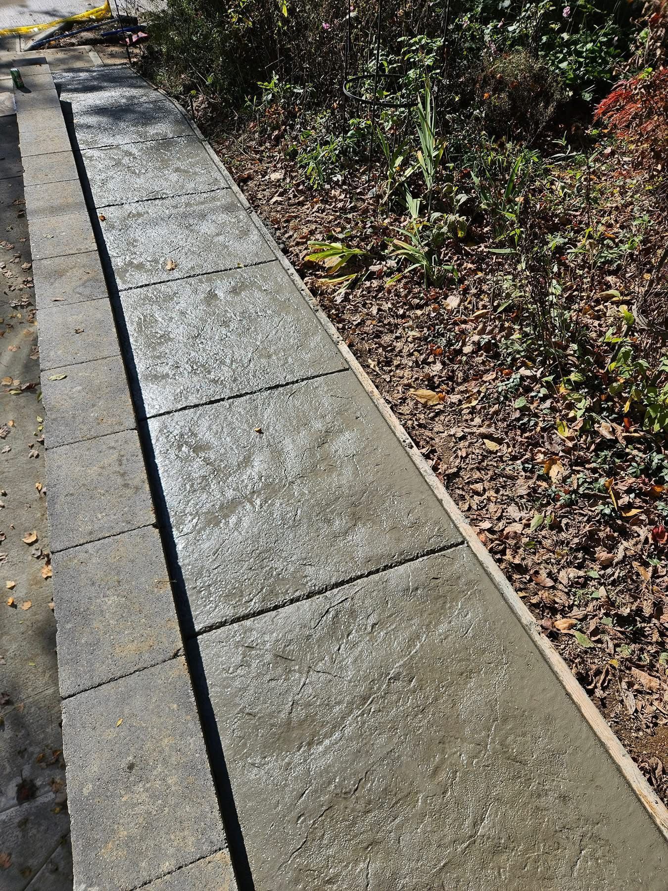 Concrete sidewalk beside a gravel garden bed, with a broken curb at the far end.