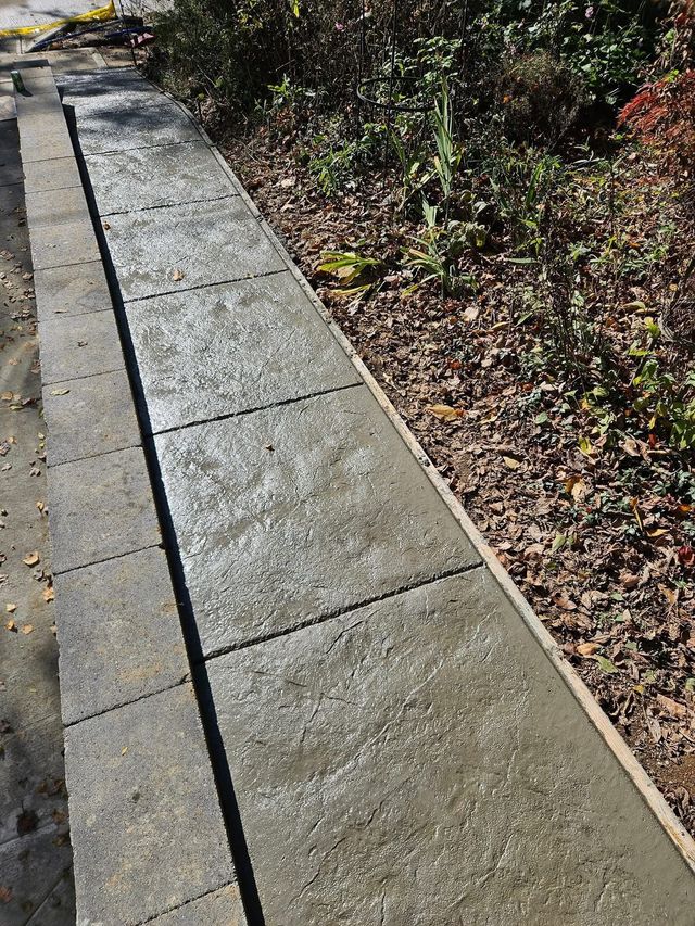 Concrete sidewalk beside a gravel garden bed, with a broken curb at the far end.