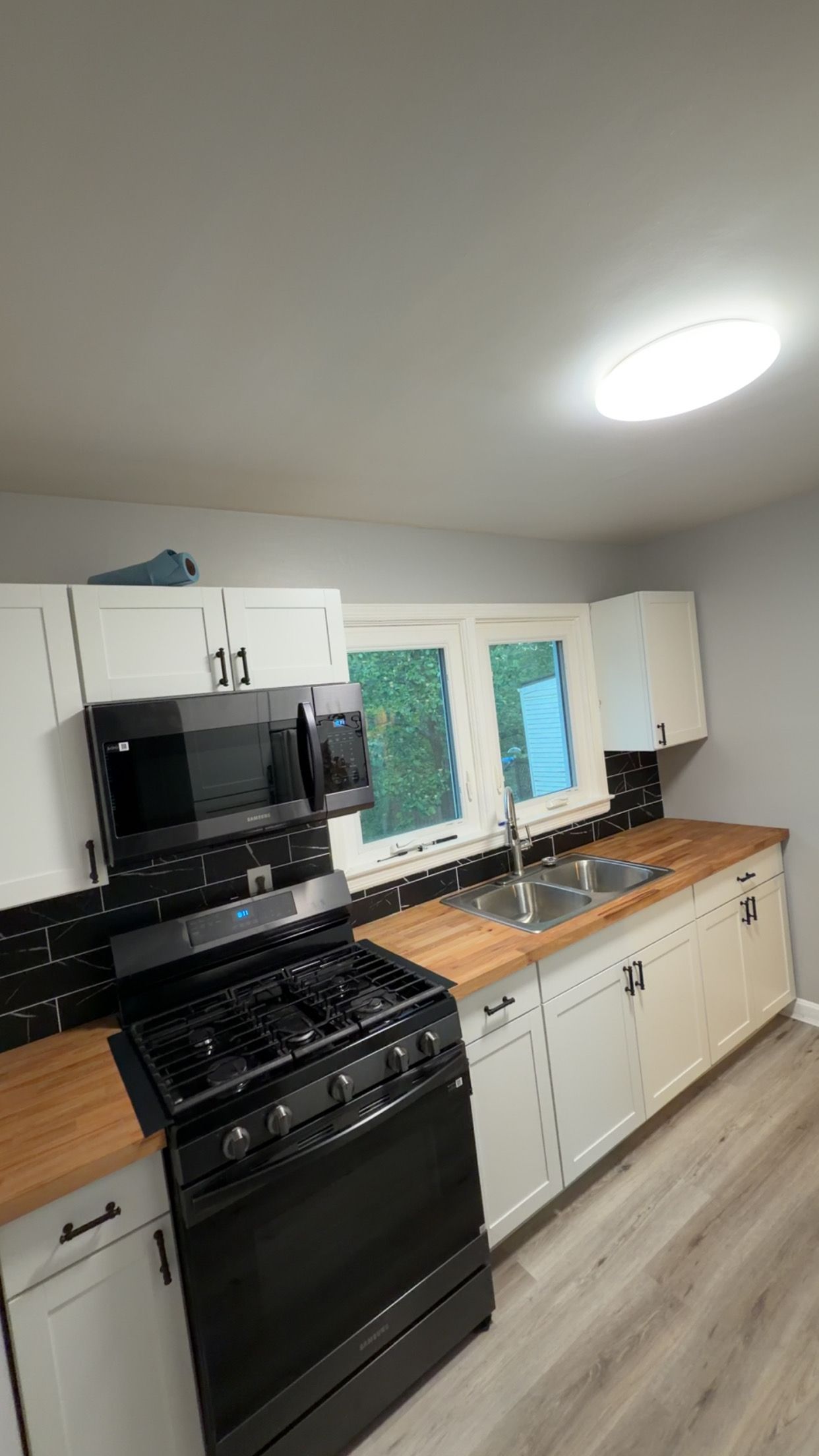 Bright kitchen with black stove, white cabinets, wood countertops, and a window over the sink.