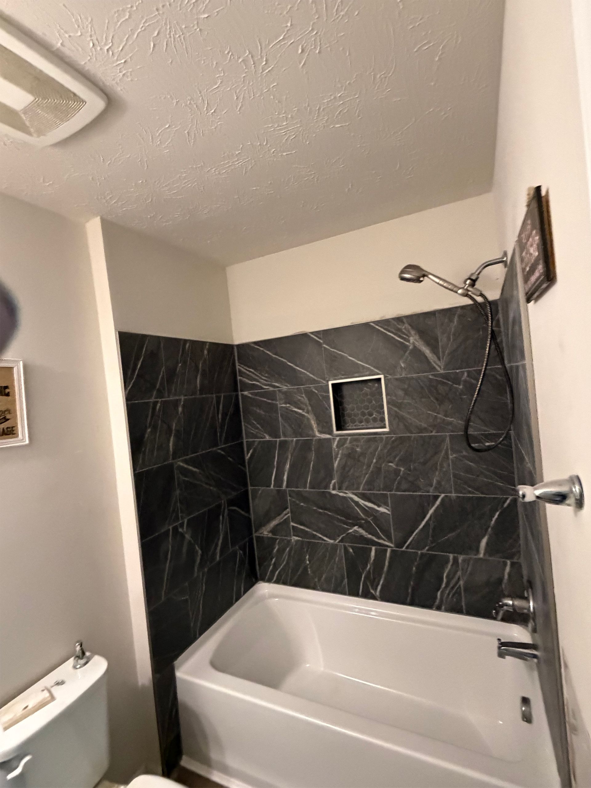 Small bathroom with a white tub, black tiled walls, and a wall-mounted shower head.