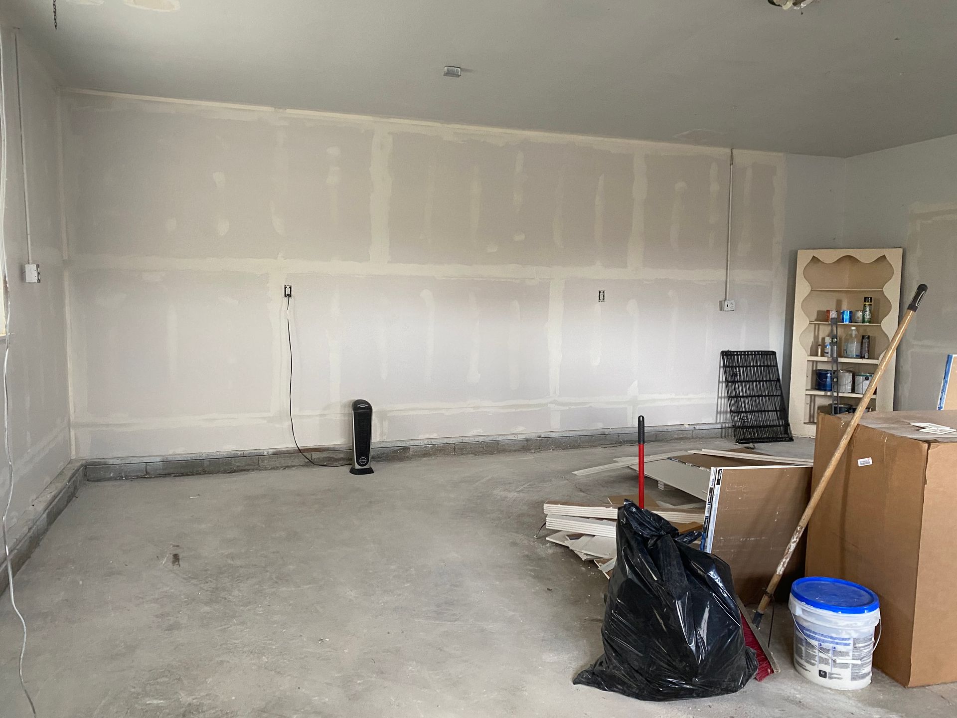 Empty garage with unfinished drywall, concrete floor, and a few tools and boxes on the right.