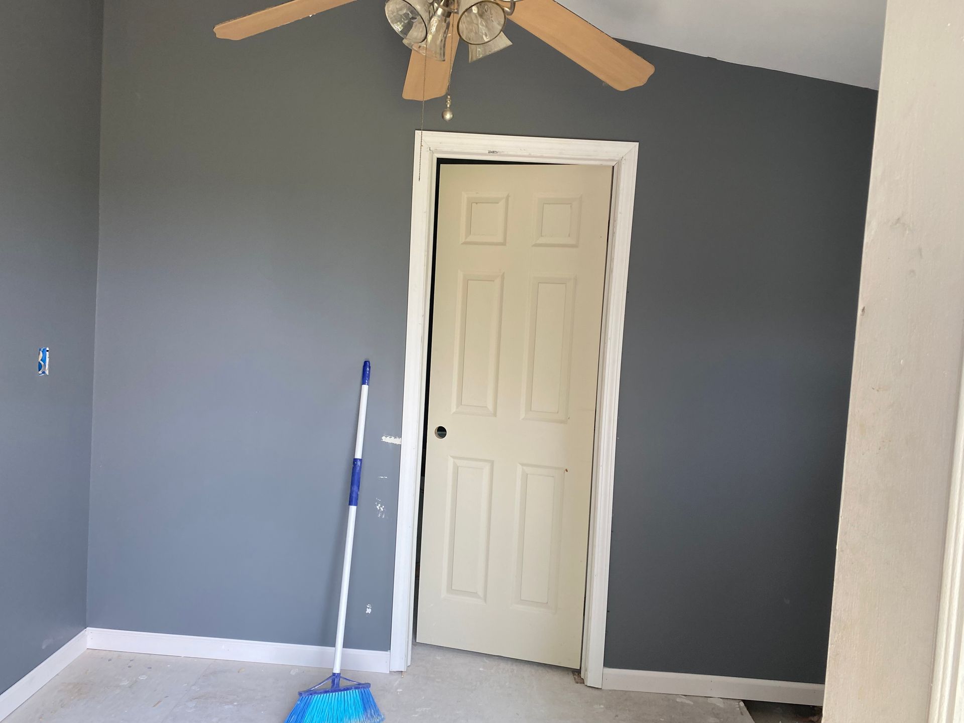 Empty room with gray walls, white door, ceiling fan, and a mop leaning by the wall.