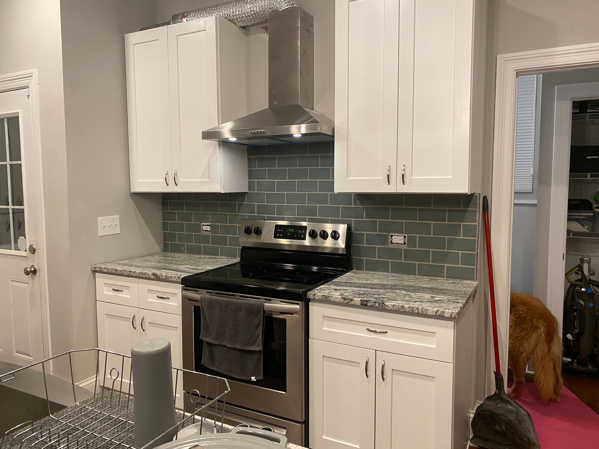Kitchen with white cabinets, stainless steel stove, green tile backsplash, and granite countertops.