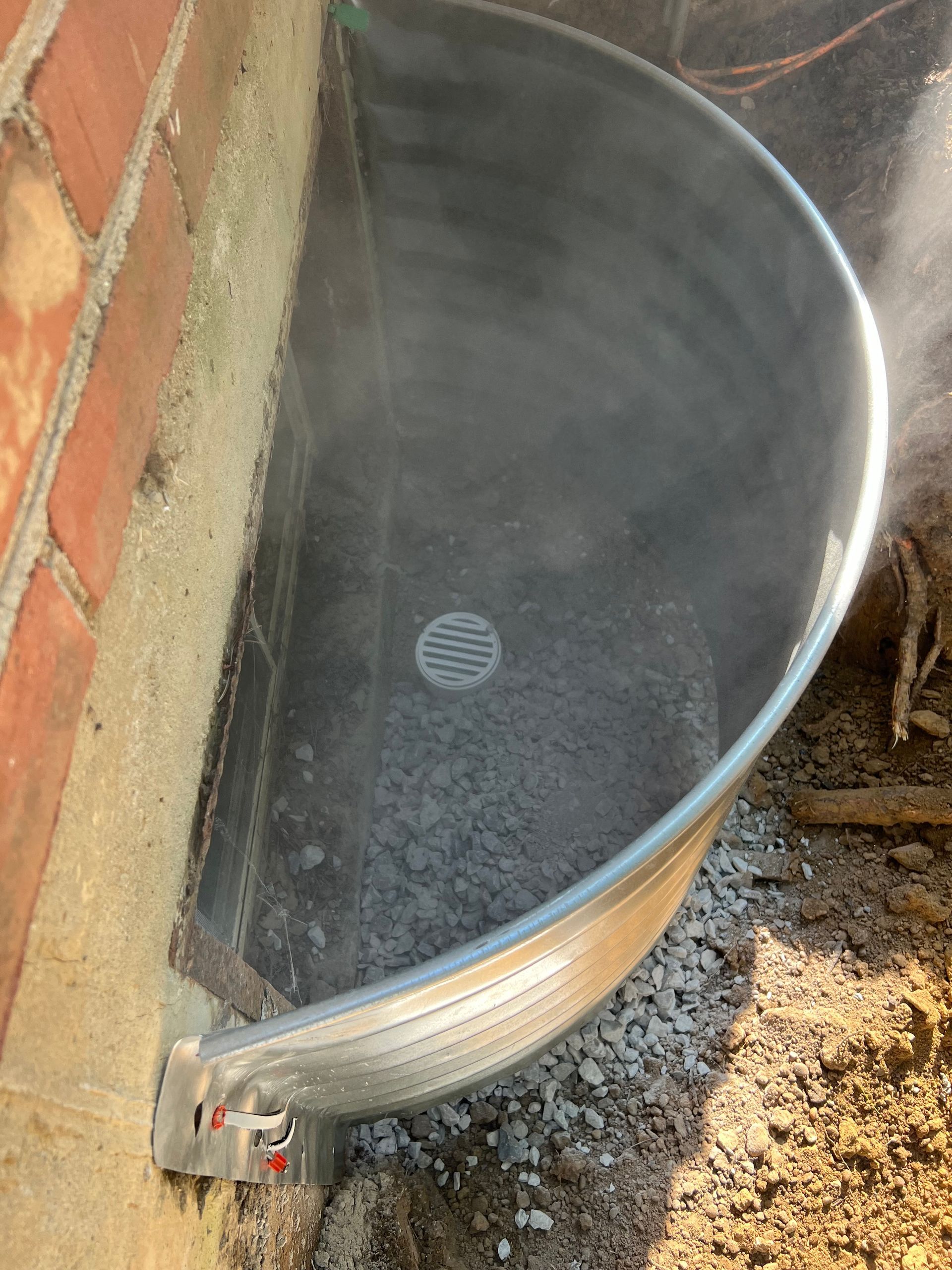 Curved metal dumpster beside a brick wall, partially filled with water and debris.