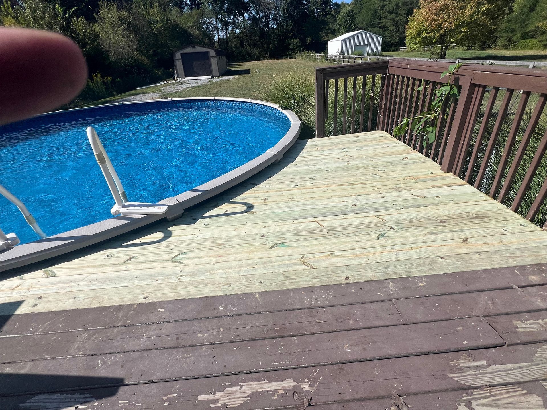 Backyard deck beside a blue above-ground pool, with a railing and green yard beyond.