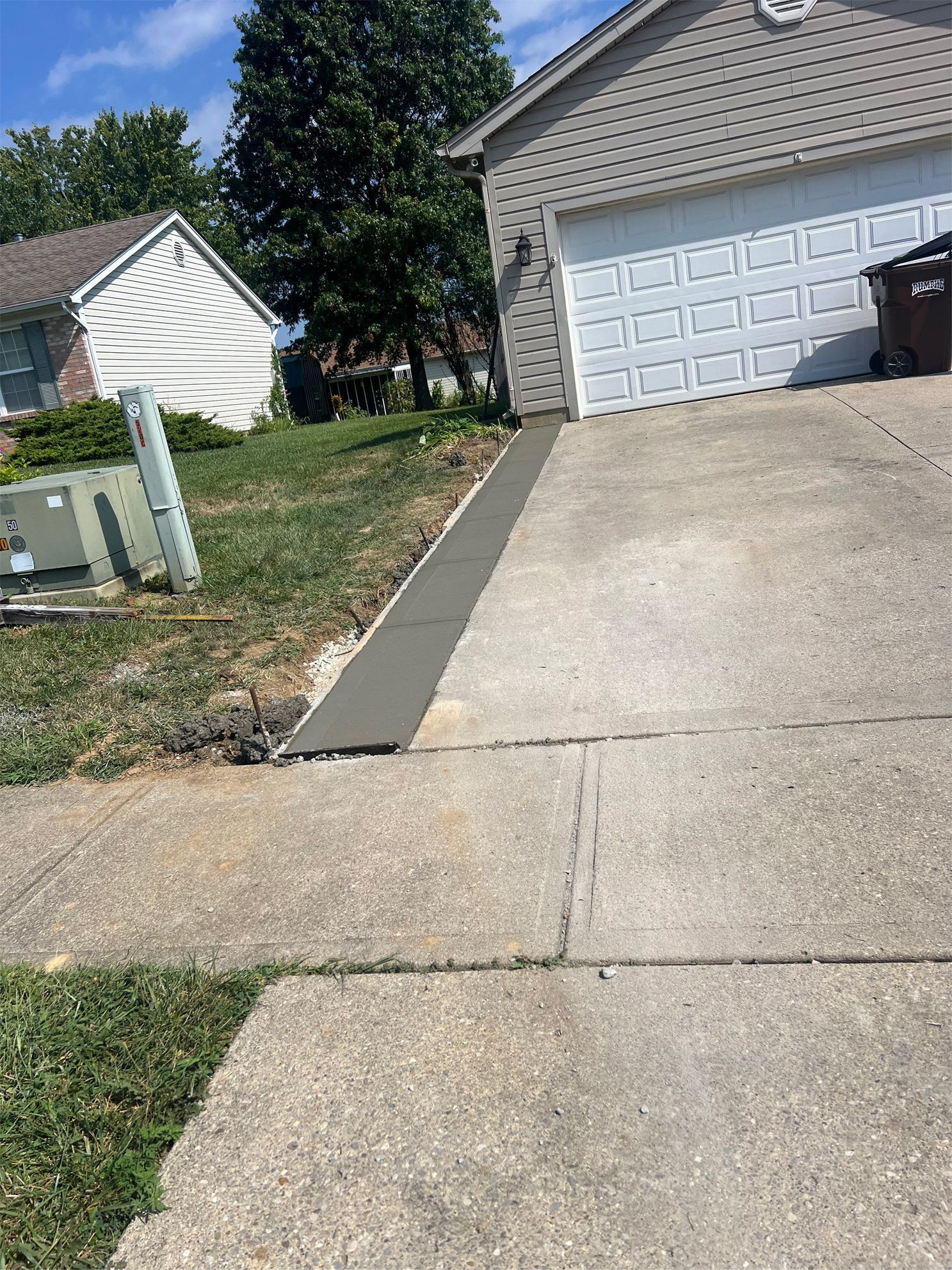 Suburban driveway leading to a two-car garage, with a concrete sidewalk and green lawn beside it.